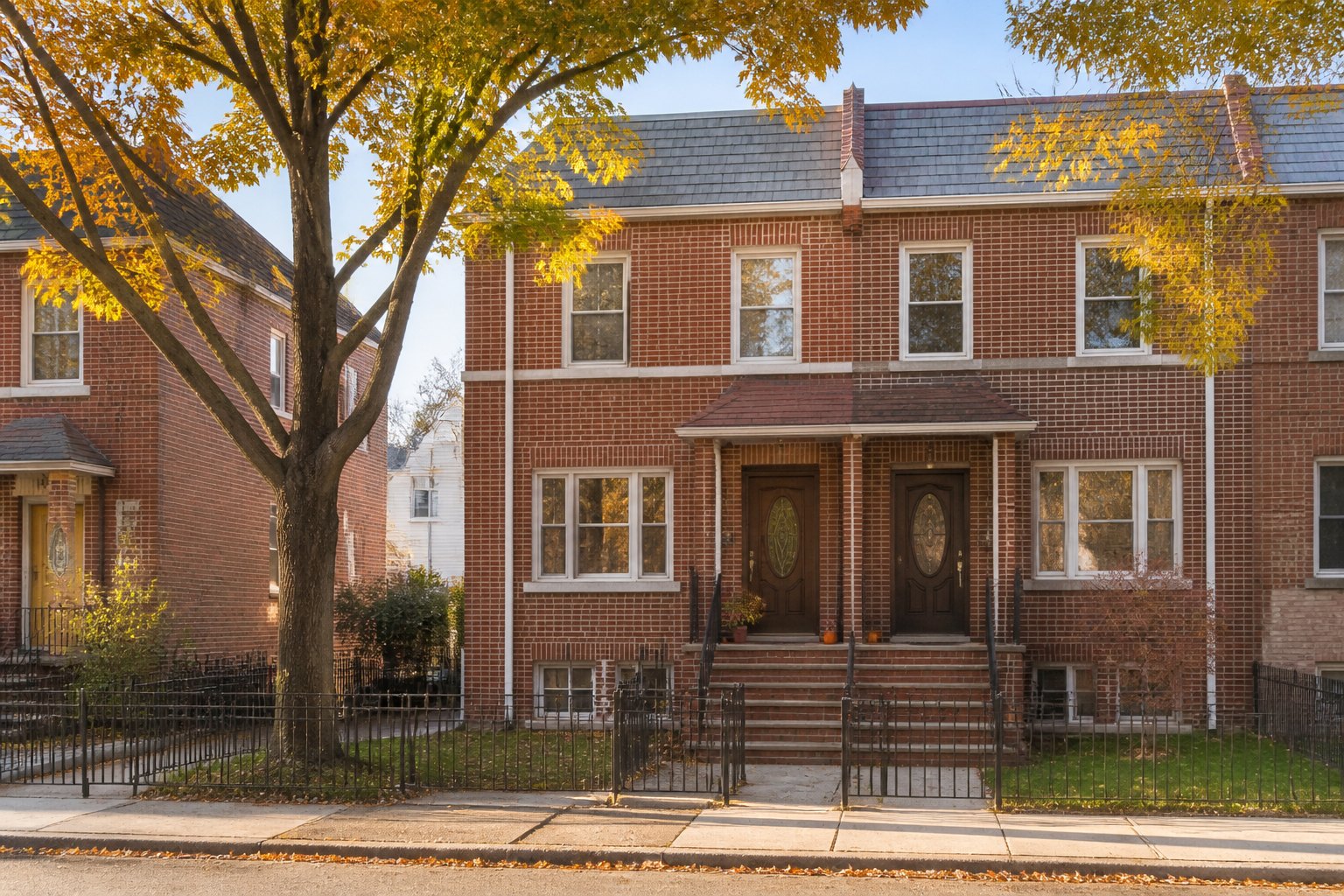 A brick two-family house with a stoop and two front doors on an autumn street, Selling a Tenant-Occupied Two-Family Home in Throggs Neck